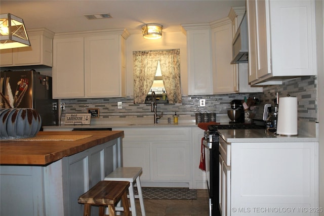 kitchen featuring backsplash, a sink, stainless steel range with electric cooktop, wooden counters, and visible vents