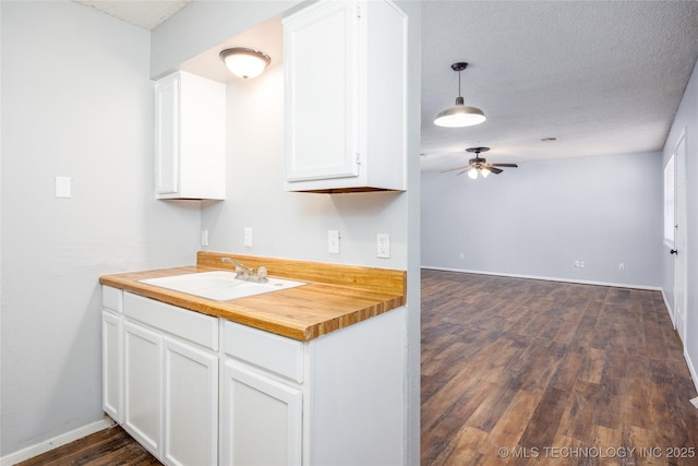 kitchen featuring a sink, a textured ceiling, white cabinetry, wooden counters, and ceiling fan