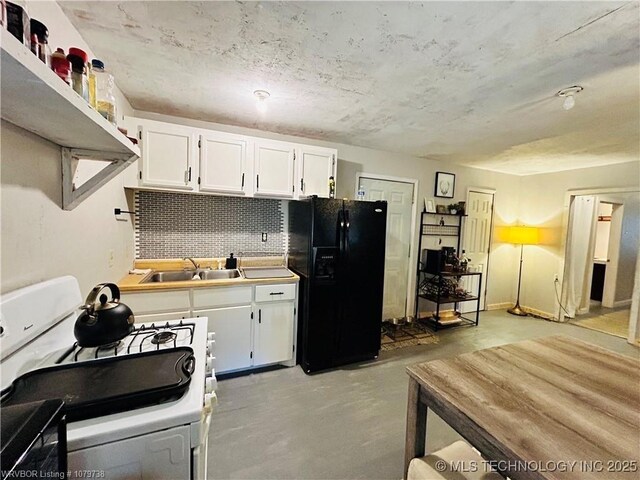 kitchen featuring concrete floors, a sink, white cabinets, black fridge with ice dispenser, and white gas range oven