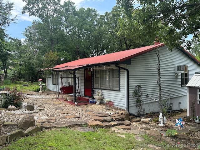 view of front facade with entry steps, metal roof, and a wall mounted AC