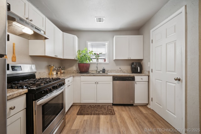 kitchen with visible vents, a sink, under cabinet range hood, stainless steel appliances, and light wood finished floors