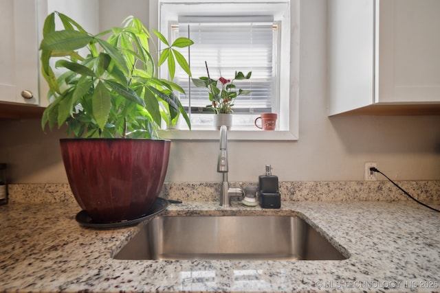 room details with white cabinets, light stone counters, and a sink