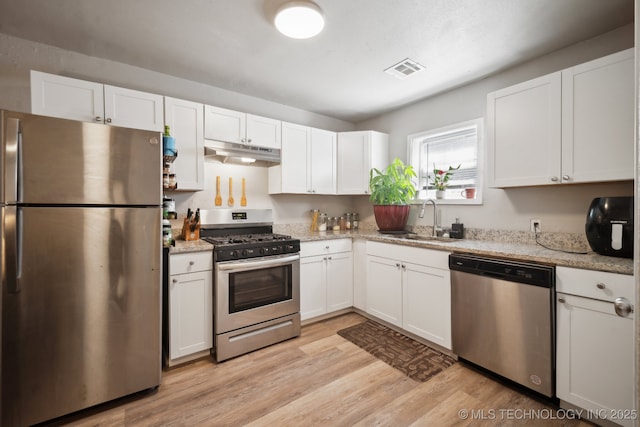 kitchen with a sink, stainless steel appliances, white cabinets, under cabinet range hood, and light wood-type flooring