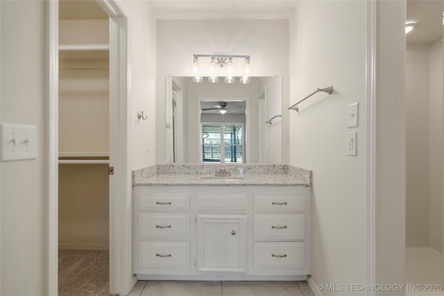 bathroom featuring a tile shower, vanity, a walk in closet, and ceiling fan