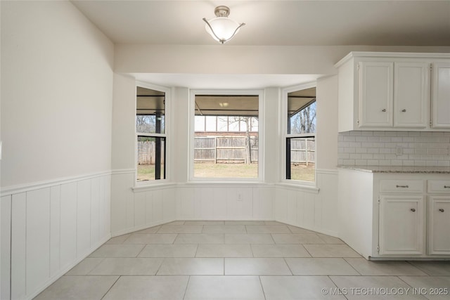 unfurnished dining area with light tile patterned floors and a wainscoted wall