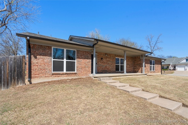 rear view of house with a yard, brick siding, and fence