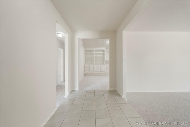 hall featuring light tile patterned floors, baseboards, and light colored carpet