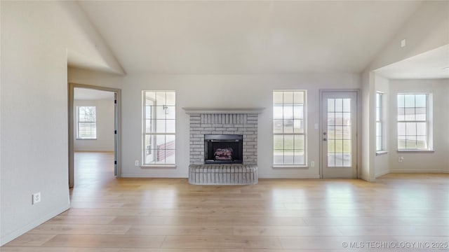 unfurnished living room featuring high vaulted ceiling, light wood-style floors, a fireplace, and baseboards