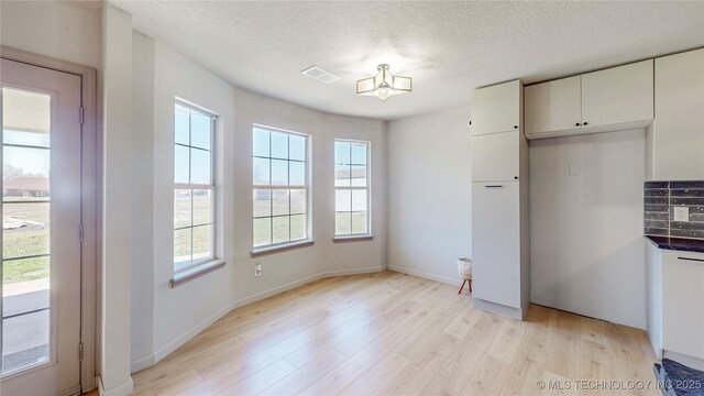 unfurnished dining area featuring a textured ceiling, visible vents, a healthy amount of sunlight, and light wood finished floors