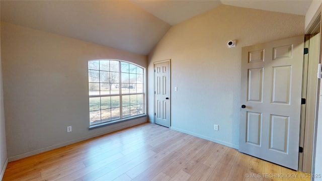 spare room with light wood finished floors, baseboards, and vaulted ceiling
