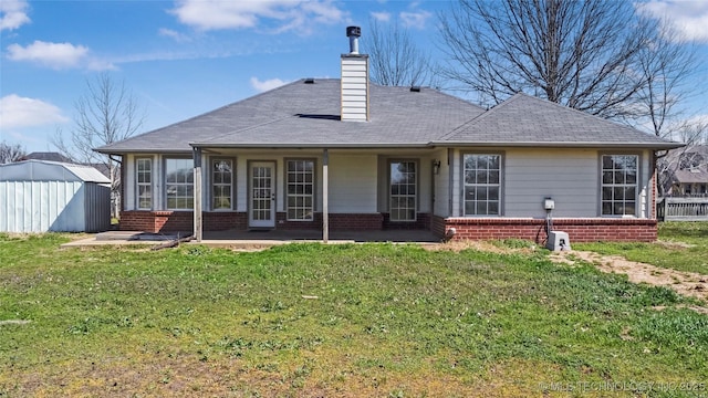 rear view of property featuring a chimney, brick siding, a storage shed, a shingled roof, and a lawn