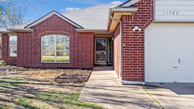doorway to property featuring brick siding, roof with shingles, and an attached garage