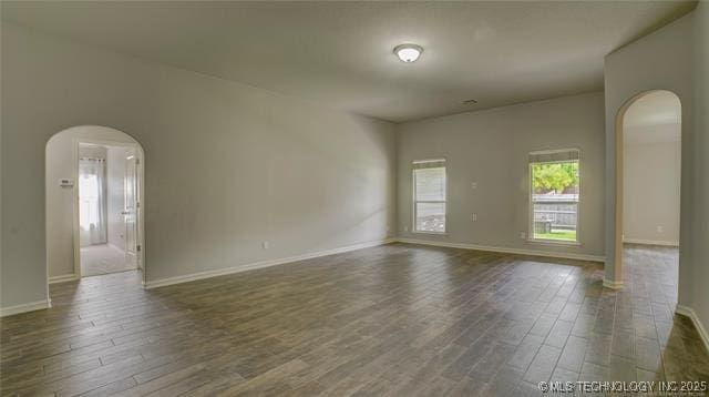 spare room featuring arched walkways, dark wood-style floors, and baseboards
