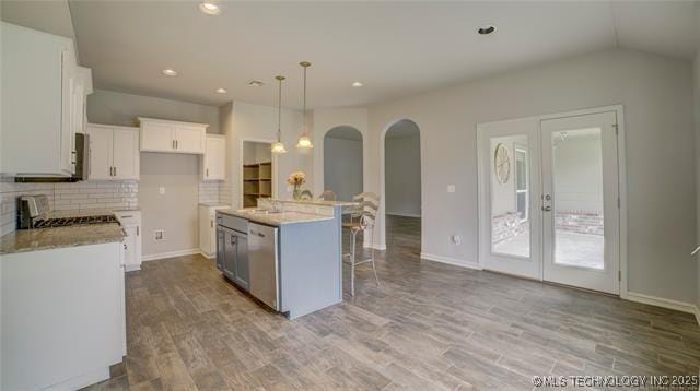 kitchen featuring white cabinets, a kitchen breakfast bar, stainless steel dishwasher, arched walkways, and hanging light fixtures