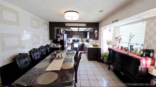 dining space featuring light tile patterned floors, visible vents, a textured ceiling, and tile walls