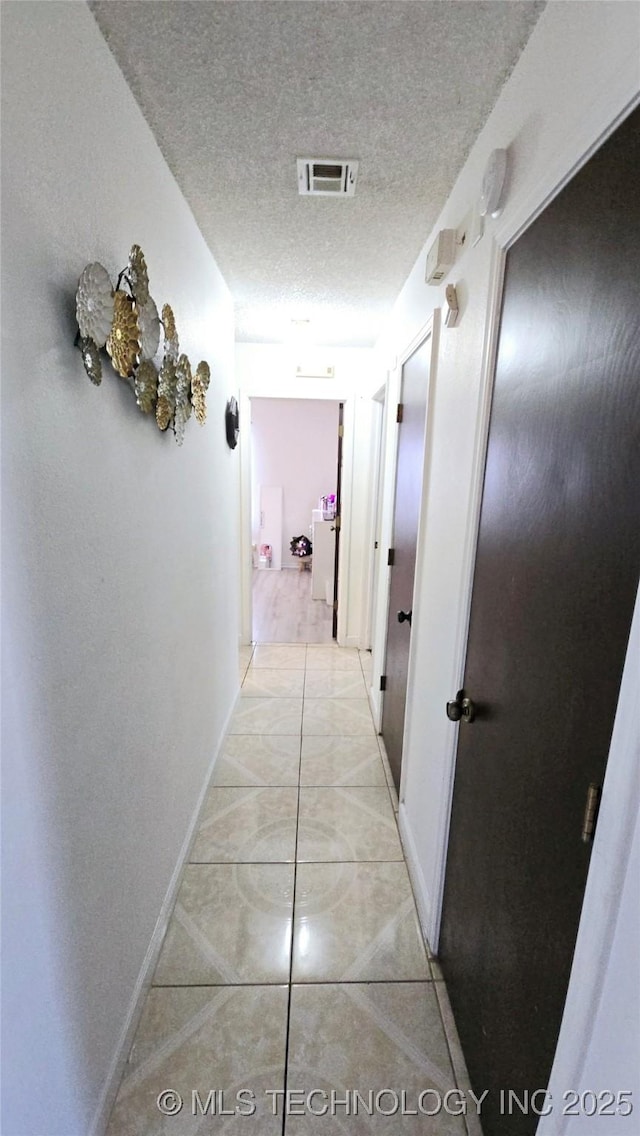 hall featuring light tile patterned floors, visible vents, a textured ceiling, and baseboards