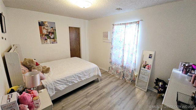 bedroom featuring visible vents, a textured ceiling, and wood finished floors