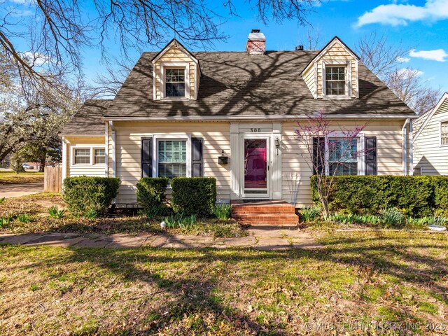 new england style home with a front lawn, roof with shingles, and a chimney