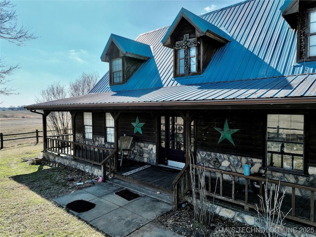 entrance to property featuring covered porch, stone siding, and metal roof