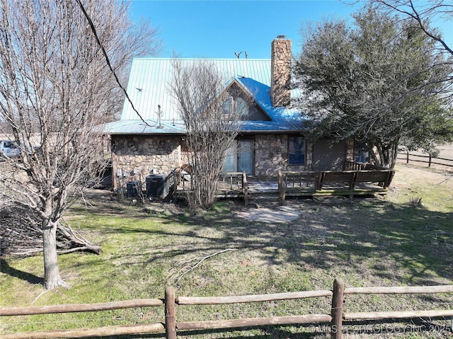 rear view of property with fence, a chimney, a deck, a lawn, and metal roof