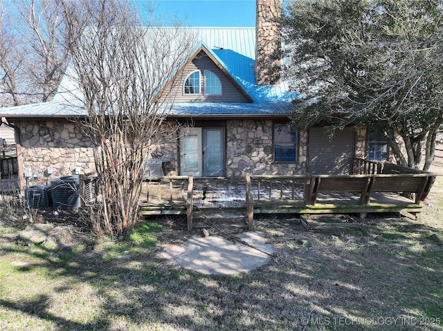 rear view of property featuring stone siding, a wooden deck, and metal roof