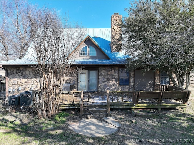 view of front facade with a chimney, metal roof, stone siding, and a wooden deck