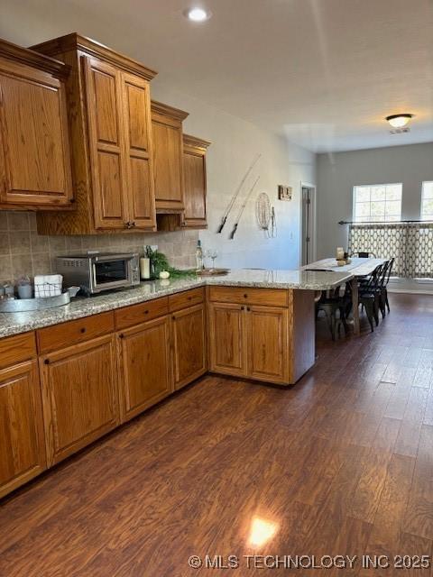 142 Elm St, Mannford, OK 74044 - kitchen with a peninsula, dark wood-style floors, brown cabinetry, light stone counters, and tasteful backsplash