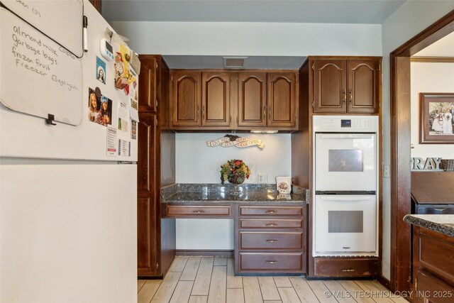 108 S Bettes Ave, Wagoner, OK 74467 - kitchen with built in study area, light wood-style flooring, dark stone countertops, and white appliances
