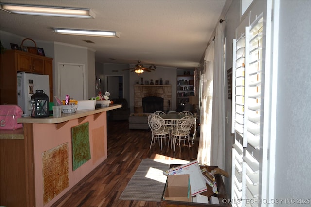 17414 Bridgeview Rd, Madill, OK 73446 - kitchen with dark wood-style flooring, a peninsula, a fireplace with raised hearth, ceiling fan, and freestanding refrigerator