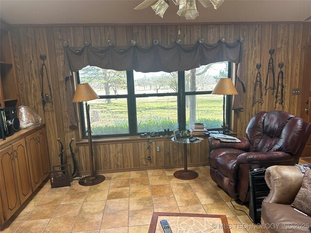 sitting room with plenty of natural light, wooden walls, and ceiling fan