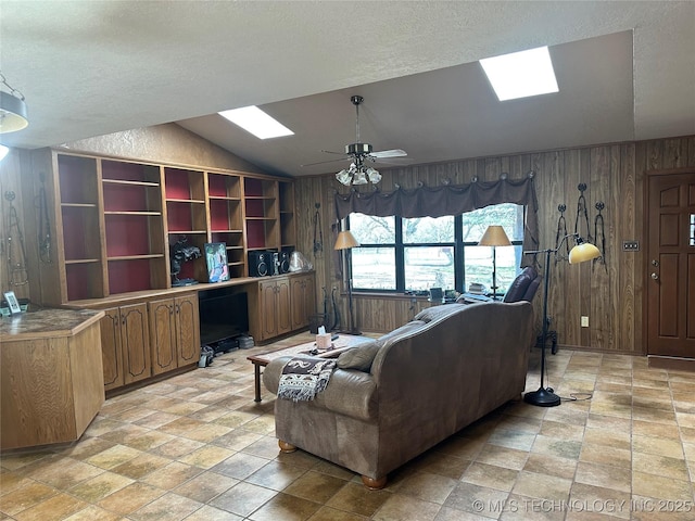 living room featuring a textured ceiling, ceiling fan, wood walls, and vaulted ceiling with skylight