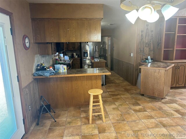 kitchen featuring a kitchen bar, stainless steel fridge, wood walls, a peninsula, and wainscoting