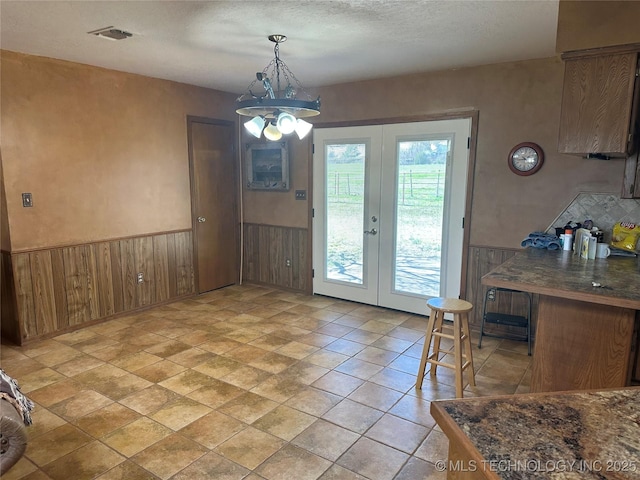 dining space with a wainscoted wall, visible vents, french doors, and an inviting chandelier