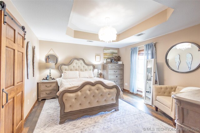 bedroom featuring visible vents, wood finished floors, a raised ceiling, a barn door, and a notable chandelier
