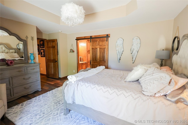 bedroom featuring dark wood-type flooring, a barn door, a tray ceiling, and a notable chandelier