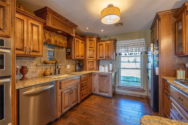 kitchen featuring a sink, stainless steel appliances, backsplash, and brown cabinets