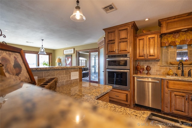kitchen featuring visible vents, brown cabinets, appliances with stainless steel finishes, a sink, and backsplash