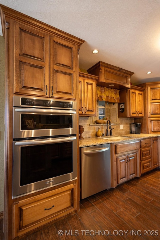 kitchen with a sink, stainless steel appliances, dark wood-style floors, and light stone counters