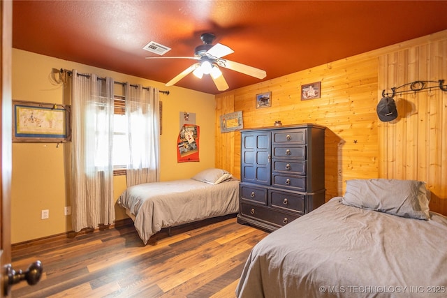 bedroom featuring ceiling fan, visible vents, wood finished floors, and wood walls