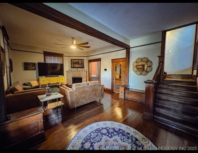 living room with ceiling fan, wood finished floors, a brick fireplace, stairway, and beam ceiling