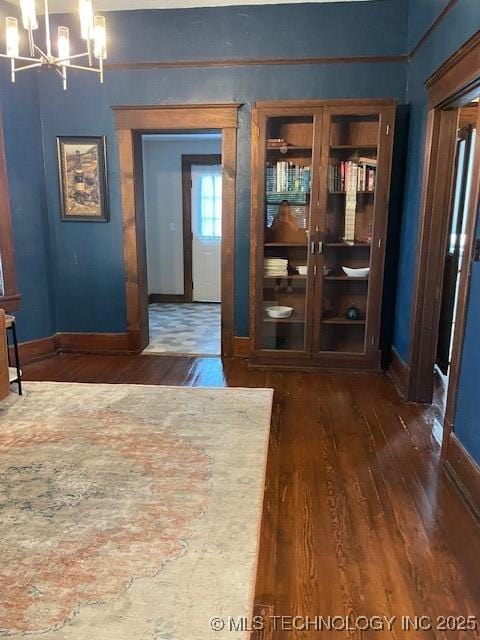 unfurnished dining area with dark wood-type flooring, a chandelier, and baseboards
