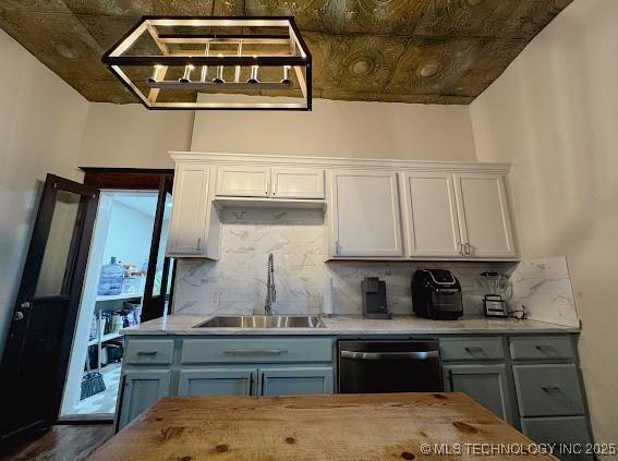 kitchen featuring tasteful backsplash, gray cabinetry, stainless steel dishwasher, and a sink