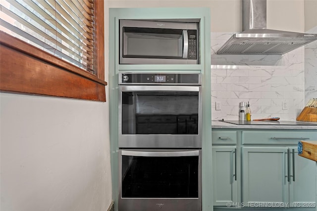 121 F SW, Ardmore, OK 73401 - kitchen featuring wall chimney range hood, appliances with stainless steel finishes, green cabinets, decorative backsplash, and light countertops
