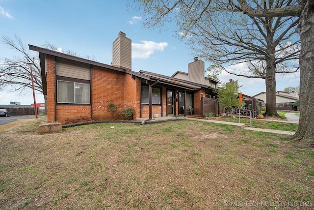 rear view of house featuring brick siding, a chimney, fence, and a yard