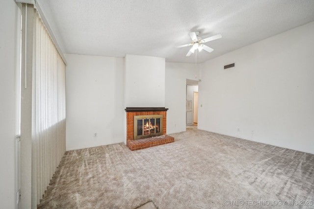 unfurnished living room featuring a brick fireplace, carpet flooring, a textured ceiling, visible vents, and a ceiling fan