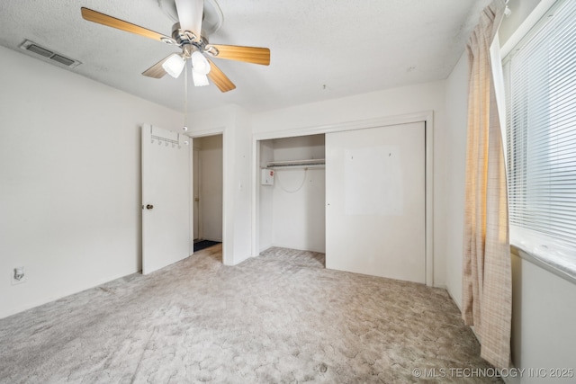 unfurnished bedroom featuring a closet, carpet flooring, a textured ceiling, visible vents, and ceiling fan