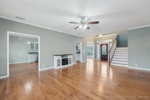 unfurnished living room with stairs, crown molding, visible vents, and ceiling fan