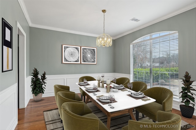 dining area featuring visible vents, wainscoting, wood finished floors, a chandelier, and ornamental molding
