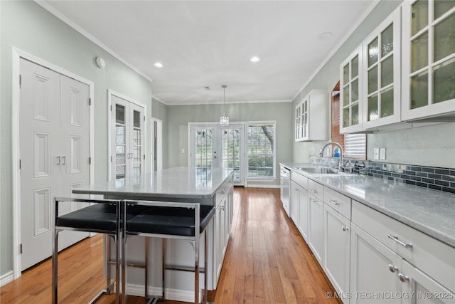 kitchen with french doors, dishwasher, a sink, ornamental molding, and white cabinetry