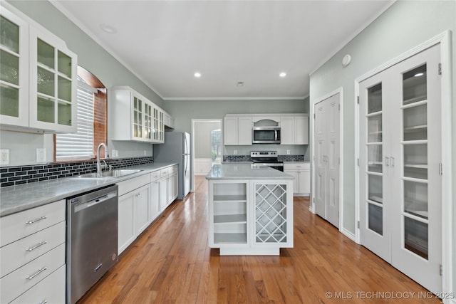 kitchen with white cabinets, a sink, light wood finished floors, stainless steel appliances, and ornamental molding